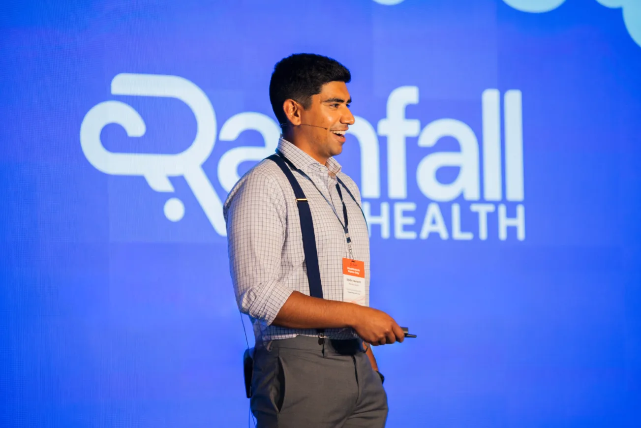 Eddie Qureshi presenting on stage in front of the Rainfall Health logo